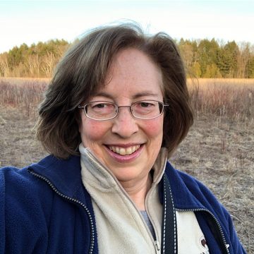 close up shot of Laurel Neme - smiling woman in fleece jacket with brown shoulder length hair and glasses standing outside in a winter marsh